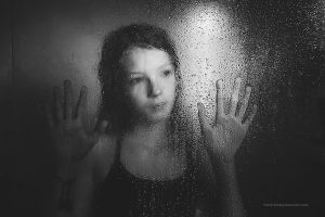 A girl stands behind a blurry, water dropped shower screen