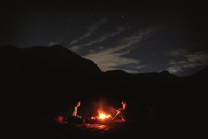 Girls sitting around a campfire in the Hajar Mountains of UAE under a starry sky