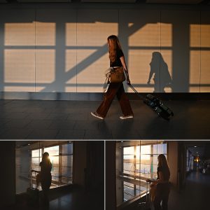 A girl walks through shadows at an airport, dragging a cabin sized suitcase